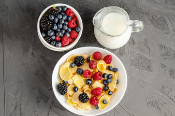 Healthy breakfast with cornflakes in a white plate, berries and milk on a dark gray background