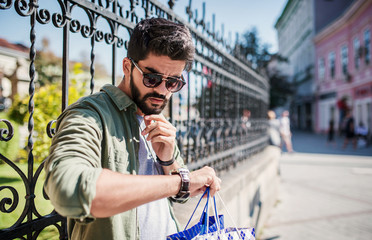 Modern young man looking at his watch while standing on the street. Shopping, lifestyle concept