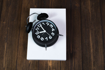 Vintage black alarm clock with white packaging gift box on dark wood table, time and deadline concept.