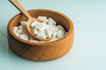 Fototapeta na wymiar White pills or tablets in wooden spoon in wooden bowl full of medications. Organic supplements and healthy life style concept.