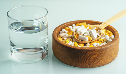 Fototapeta na wymiar Lot of healthy supplements in wooden bowl and glass of water. Nutrition diet and organic medications.
