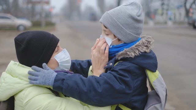 Protection against Chinese coronavirus in a European city. Mom corrects a protective medical mask to a little son on the street.