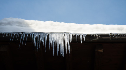 Bright icicles on the corner of a roof in a chilly day. Snow on the top