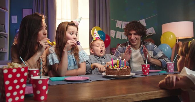 Portrait shot of the cheerful Caucasian family celebrating birthday of the small son while boy blowing candles on the cake.