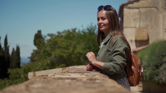 Beautiful girl walks up to stone parapet of medieval fortress and looks on vie