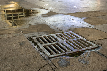 grid manhole on street at night and wet sidewalk in downtown Sao Paulo, Brazil
