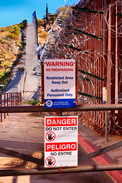 Warning signs in both English and Spanish at the US-Mexican border wall with layers of razor wire at Nogales AZ