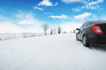 Car on the winter countryside road with snow against a sky with clouds