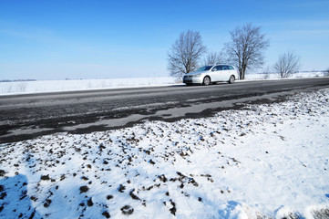 Car on the winter countryside road with snow against sky
