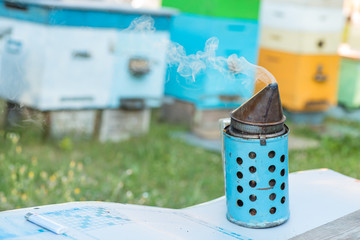 bee smoker against backdrop of apiary with colorful beehives. Smoke from bee smoker is used to calm...