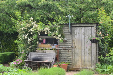 Wooden bench flower hanging basket weather vane garden potting and storage shed in the English...