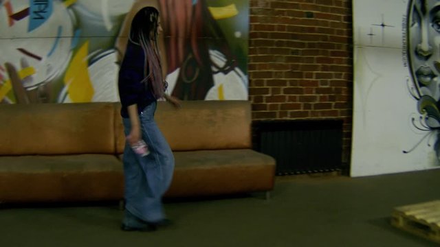 Woman with dreadlocks on graffiti background. Stock footage. Beautiful stylish woman in vintage style walks on background of brick walls with graffiti
