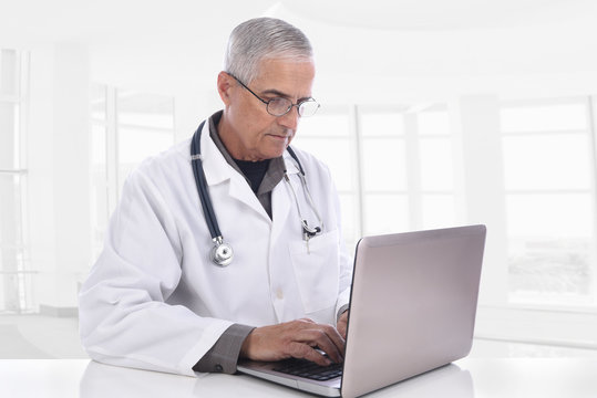 Portrait of a mature caucasian doctor at his desk with his laptop computer. Isolated on white.