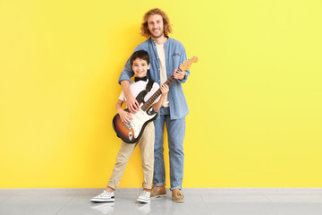 Man and his little son with guitar near color wall
