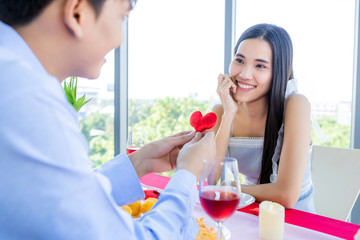 Valentine's day concept,asian Young happy sweet couple show in love show holding Small a red heart shaped pillow After lunch In a restaurant background