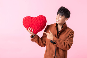 Valentine's day concept, Asian a man handsome young holding a red heart shaped pillow in love isolated on pink blank copy space studio background.