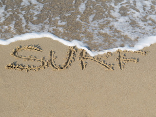 Sandy beach with wave and the written in sand word Surf.