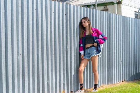 Modern teenage girl standing by corrugated iron fence background.
