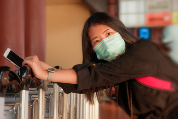 young beautiful Asian Chinese student woman at airport wearing protective facial mask checking news...