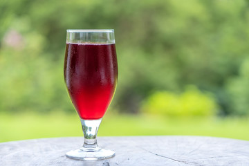 Glass with tropical red juice from leaf hibiscus on the wooden table in yard, close up, Tanzania, Africa, copy space