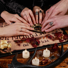 People conducting a seance using a Ouija Board, or Talking Spirit Board, with white candles. Shot...