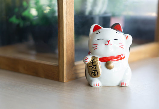 Maneki neko lucky cat show text on hand meaning rich on wood table background, select focus