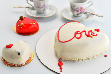 St. Valentine's Day background for bakery, confectionery.  White  mousse cake  and two little cakes in the shape of a heart  on a white background.  .