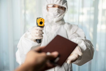 Airport security wearing gloves with biohazard chemical protective suit and mask, Check at gates with digital thermometer checking temperature.
