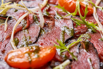 Closeup Beef carpaccio with pesto sauce and tomatoes on black table. Restaurant menu, natural and organic food concept.