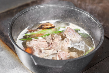 Traditional beef broth with vegetable, bones and ingredients in pot, cooking recipe. Soup in a cooking pot with ladle on dark stone background. Top view