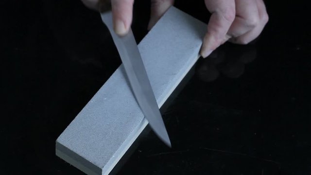 knife sharpening on Whetstone on background of black boards.