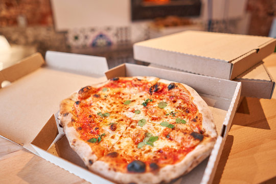 Pizza delivery concept. Baked products in a cardboard box against a wooden background. Baked tasty margherita pizza in Traditional wood oven in Neapolitan restaurant, Italy.