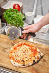 Italian kitchen and cooking concept. Chief with a pizza cutter cutting pizza to pieces at Neapolitan pizzeria.