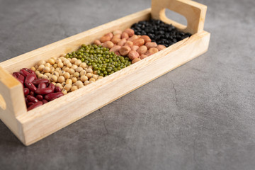 Grains or beans, red bean, black bean, green bean, soybean, peanut in the wooden tray placed on the black cement floor. High angle view.