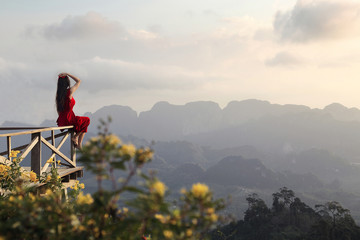 Rear view of a female tourist in a red dress sitting and watching the beautiful scenery during sunrise of Doi Tapang (Doi Ta Pang) Viewpoint at Chumphon province in Thailand.