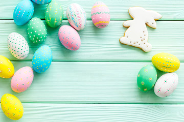 Easter symbols. Painted eggs and bunny gingerbread on green wooden desk top-down frame copy space