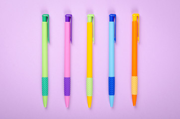 Different colored pens, school ballpoint on purple background composition.