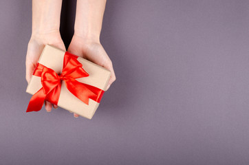 Hands with gift box on dark background composition, present with ribbon and bow.
