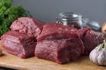 pieces of raw beef on a cutting board, next to herbs and spices, cooking