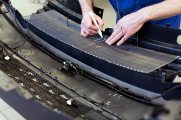 Hands of a professional mechanic at work. Trimming the mesh from stones falling into the front bumper of the car. Car tuning in a car service.