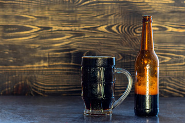 wooden background, mug and bottle of dark beer with foam. Copy space. Close-up.