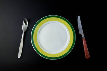 Fork, knife and empty green plate on a black background
