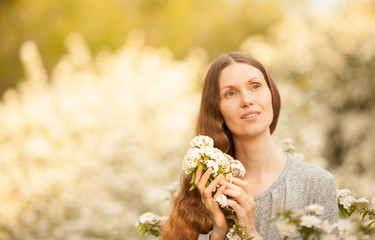 A beautiful woman in the spring in a blooming garden, holding flowers in her hands, looking dreamily at the sky, smiling. Beautiful close-up portrait. Concept: spring. March 8. Natural beauty.