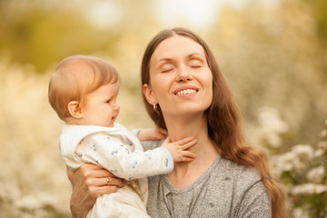 Beautiful young, happy woman with a baby in the spring in a blooming garden, smiling. Place for the inscription. Concept: spring. Happiness. Mother's day. Relationships in the family. March 8.