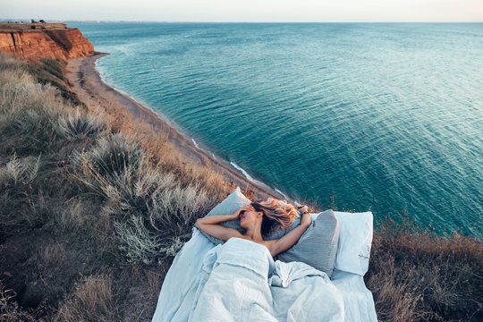 Woman enjoying view on beach landscape while relaxing in bed in sunset on the edge of Earth