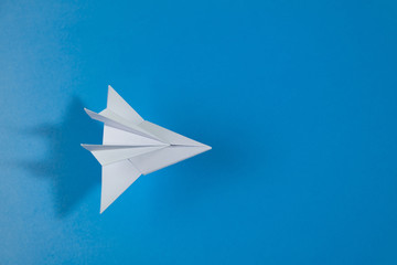 White paper jet flies above blue background. Top view