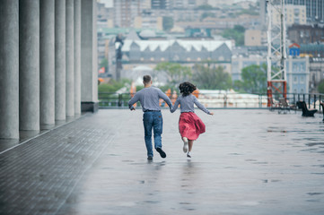 a pair of lovers in striped sweatshirts run away from everyone holding hands on a wet rainy day on a city street