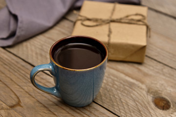 Cup of black coffee on wooden table next to present wrapped into craft paper