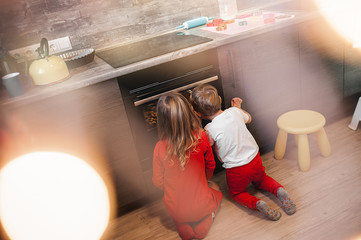 brother and sister look into the oven in the kitchen and expect to make a Christmas cake, family...