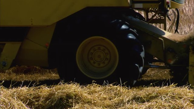 Close-up side view sunny day low angle still shot of a yellow combine harvester harvesting wheat, and removing chaff and stalks at the back, countryside scene, Europe